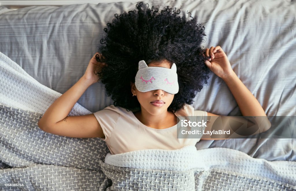Do not disturb Shot of a young woman sleeping with a mask on in bed Sleeping Stock Photo