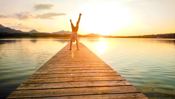 istock Woman Doing Handstand On Pier Over Lake During Sunset 1058395770