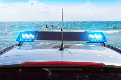police car with blue flashing lights on the beach against blue sea and sky