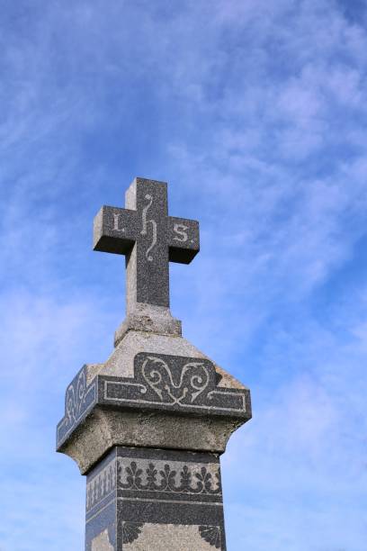 istock Stone grave marker with cross on top with blue sky in background 1058400386