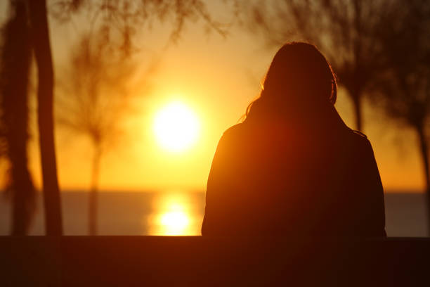 silhueta de uma mulher solitária, assistindo o pôr do sol no inverno - sun watch - fotografias e filmes do acervo