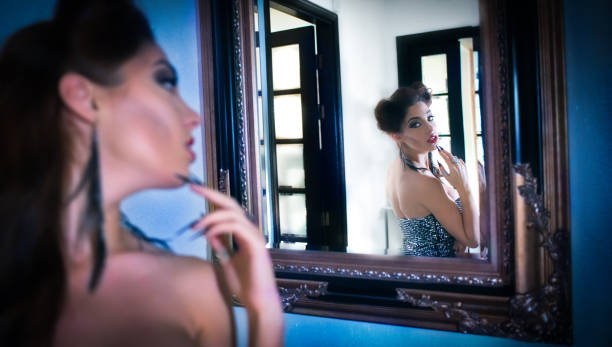 istock Beautiful woman model  looking like a vampire, seeing her reflection in the mirror, with stiletto fingernails on her face, big black eyes, big hair and red lips. Maleficent lookalike and Halloween concept 1058403250