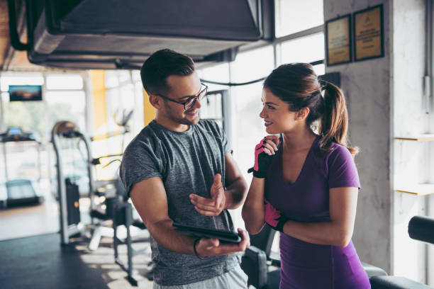 mujer sonriente y plan de ejercicio que hace de entrenador personal en gimnasio - gym machine smiling coach fotografías e imágenes de stock