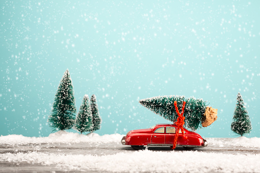 Red toy car carrying a Christmas tree in a snowy landscape. Space for text.