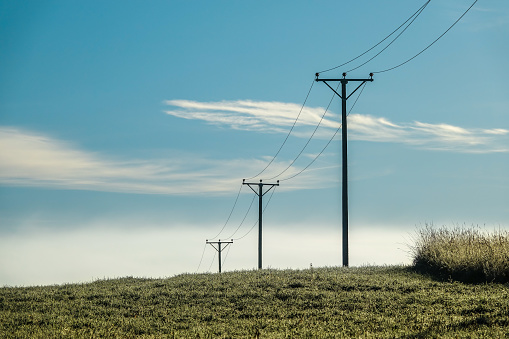 Electrical power line over the field. Blue sky, fog and green grass, early morning in autumn.