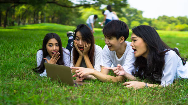 istock Shocked Friends Looking At Laptop While Lying On Grassy Field At Park 1058423998