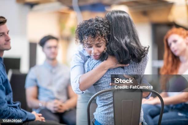 Two Women Hugging During A Support Group Meeting Stock Photo - Download Image Now - Group Therapy, Group Of People, Psychotherapy