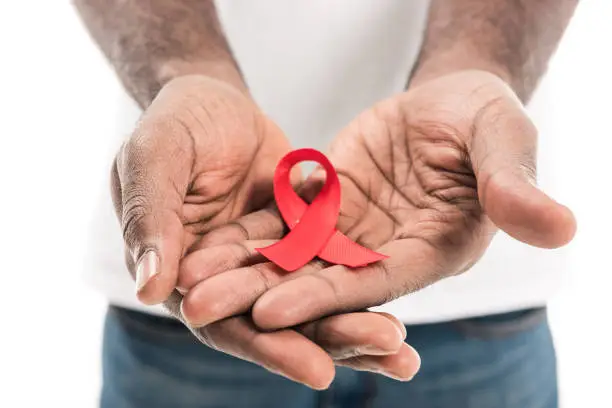 Photo of cropped shot of african american man holding aids awareness red ribbon isolated on white