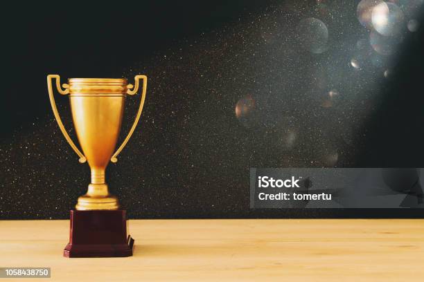 Low Key Image Of Gold Trophy Over Wooden Table And Dark Background With Abstract Glitter Lights Stock Photo - Download Image Now