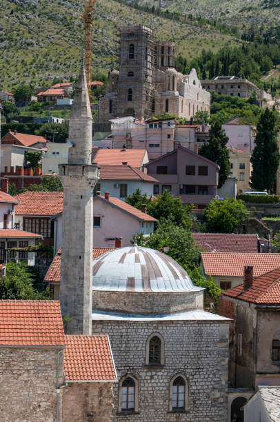 Bosnia: view of the Clock Tower (Sahat Kula), example of the proliﬁc Ottoman period, dated 1630, bombed and damaged during the Bosnian War (1992-1995), and a mosque with its minaret Mostar, Bosnia and Herzegovina, Europe - July 5, 2018: view of the Clock Tower (Sahat Kula), example of the proliﬁc Ottoman period, dated 1630, bombed and damaged during the Bosnian War (1992-1995), and a mosque with its minaret ethnic cleansing stock pictures, royalty-free photos & images