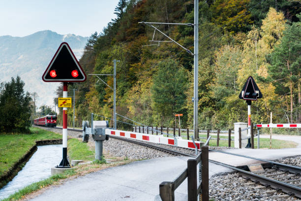 railraod crossing with blinking warning lights and a red train approaching in the Swiss countryside in the Landquart region of the Grisons