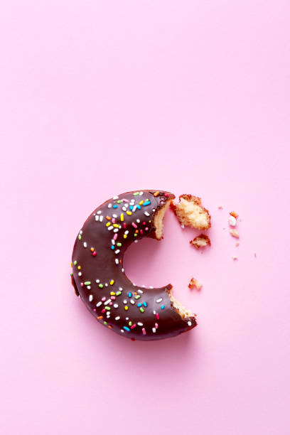 Half eaten donut with chocolate coating and sprinkles on a pink background viewed from above. Sweet food leftovers. Top view. Copy space stock photo