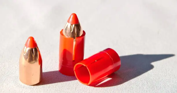 Two muzzleloader sabot bullets, one within a plastic casing used to shoot it with and the other without. An unloaded casing is shown as well as shadows