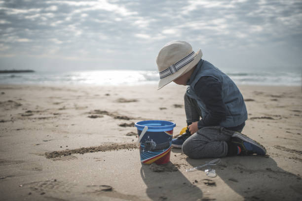 Little boy having fun at beach. Boy is running with a bucket of water and splashing. Sunny summer day.\n