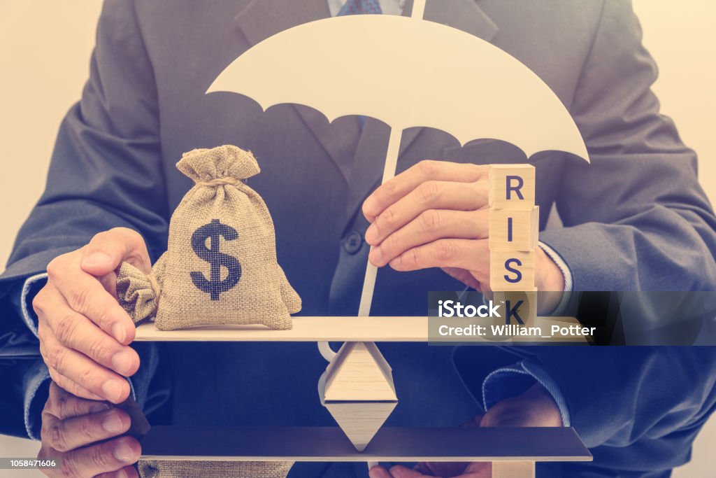 Financial risk assessment / portfolio risk management and protection concept : Businessman holds a white umbrella, protects a dollar bag on basic balance scale, defends money from being cheat or fraud Risk Stock Photo