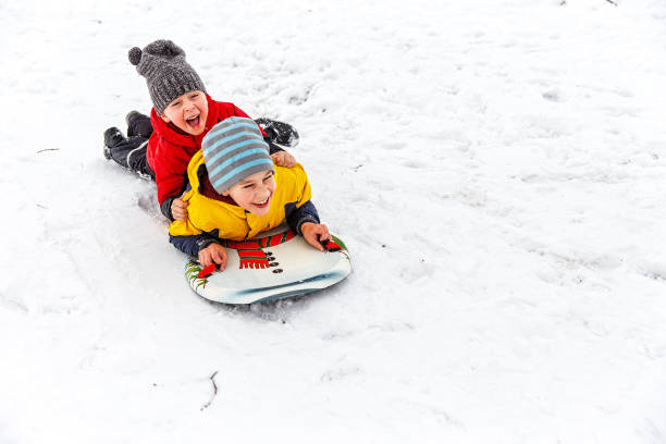 happy children having fun sliding down the hill excited kids laughing in the snow. Cope space for your text children in winter stock pictures, royalty-free photos & images