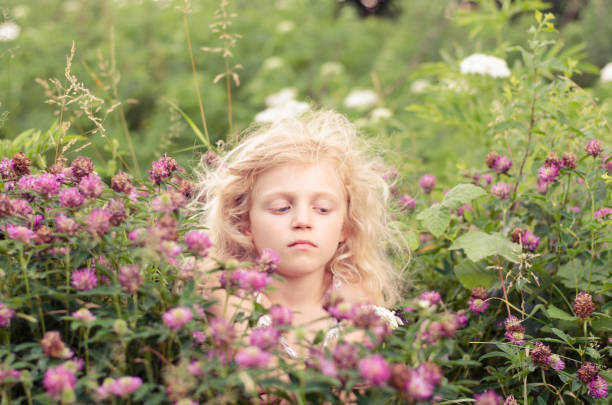 little blond girl with pink clover flowers around in the meadow