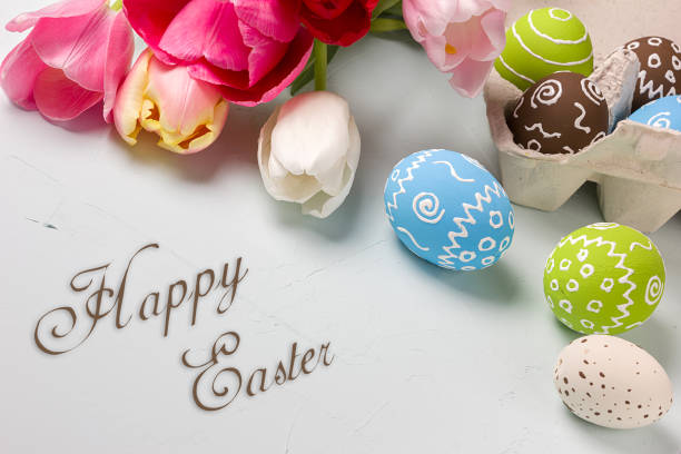 istock Painted easter eggs and bouquet of spring tulips closeup on a light blue background with space for congratulation 1058478810