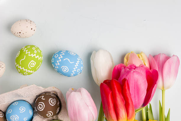 istock Painted easter eggs and bouquet of spring tulips closeup on a light blue background with space for congratulation 1058478982