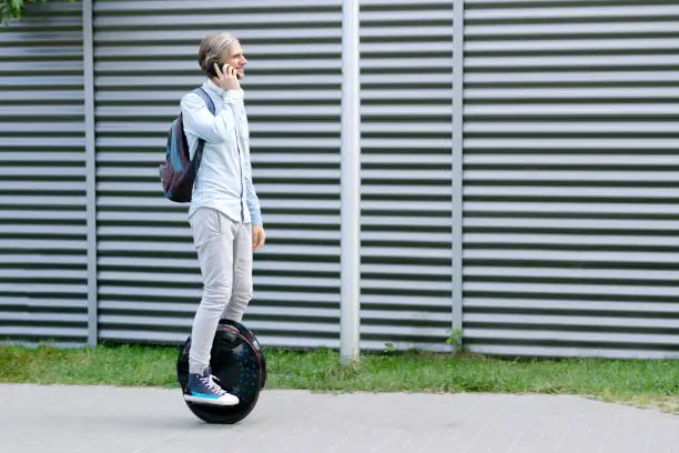Modern young adult male businessman student freelancer riding driving on ecological electric transport futuristic eco electric unicycle scooter, balancing electric wheel with smartphone. Eco planet.