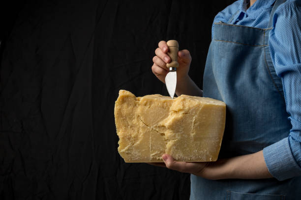 Woman holding knife and a slice of parmesan cheese on black background stock photo
