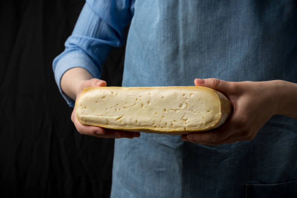 Woman in blue apron holding taleggio cheese on dark background Woman in blue apron holding taleggio cheese on dark background. Studio shot dairy producer stock pictures, royalty-free photos & images