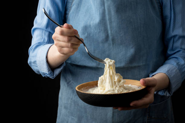 istock Woman in blue apron holding bowl with stracciatella mozzarella cheese on dark background 1058507214