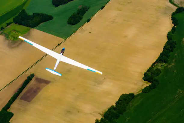 A glider in flight over green and brown fields