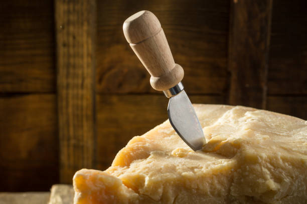 Parmesan cheese with knife on wooden board on dark background stock photo
