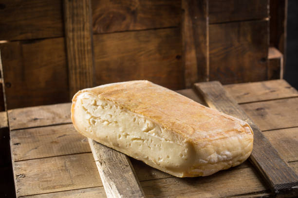 Piece of taleggio cheese on wooden board on dark background stock photo