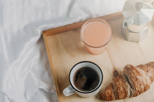 istock Breakfast in bed on white silky linen. Croissant, coffee and juice Window light 1058519922