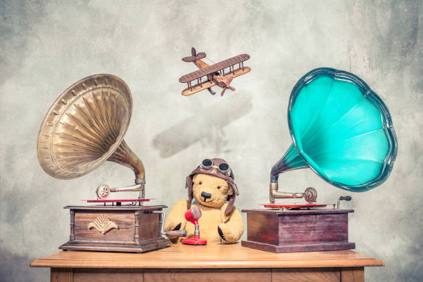 teddy bear with aviator's helmet and goggles, aged antique gramophone phonograph turntables with old retro microphone, flying toy plane with its shadow on concrete wall. vintage style filtered photo - radio 1930s imagens e fotografias de stock