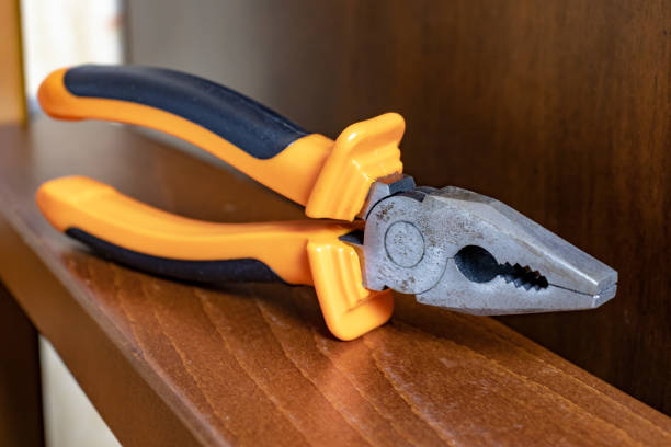 istock Pliers with orange handles on brown wooden plank 1058528482