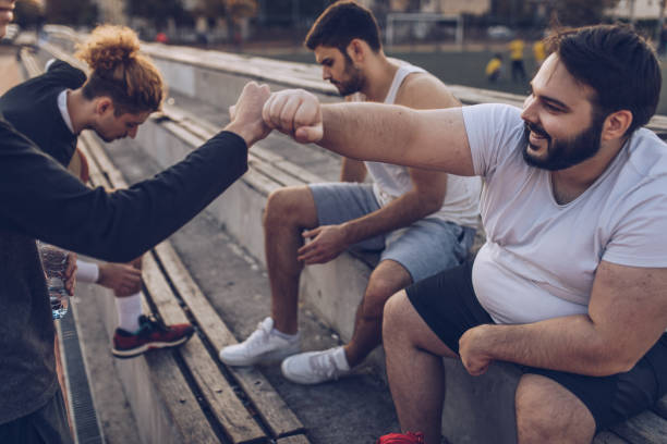 Basketball friends relaxing Group of men, street basketball friends sitting on bleachers on a sunny day outdoors, taking a break. basketball sport photos stock pictures, royalty-free photos & images