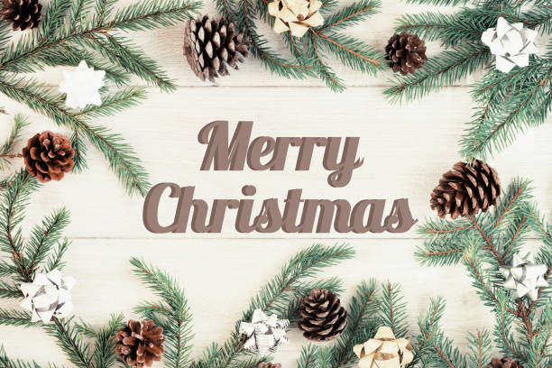 istock Christmas composition, frame. Spruce branches decorated with gold and silver bows and cones, laid out in a circle. In the center of the inscription Merry Christmas. Festive photo on a light wooden background. 1058540426