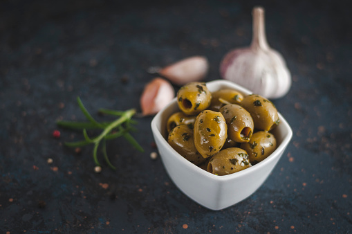 Fresh olives in olive oil on rustic background. Olives with garlic bulb, pepper and rosemary.