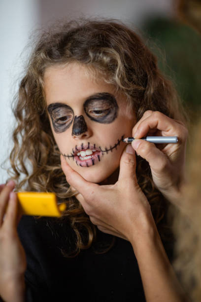 mała goth dziewczyna kładąc makijaż na twarzy, patrząc w małym żółtym lustrze - face paint human face mask carnival zdjęcia i obrazy z banku zdjęć