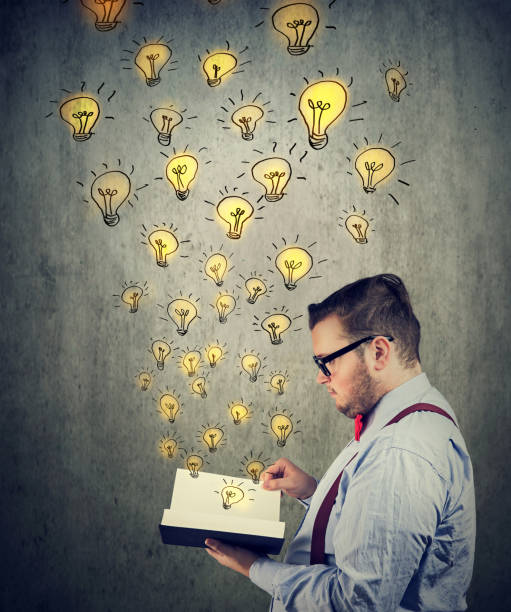 istock Businessman holding reading an opened book with glowing light bulbs flying out 1058575348