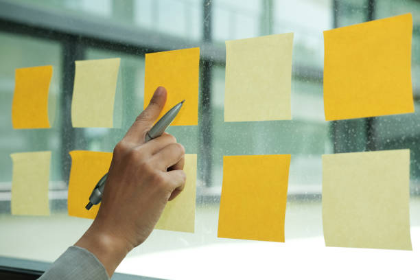 istock hand pointing at adhesive notes on glass wall. Sticky note paper reminder schedule for creative idea & business brainstorming 1058582682