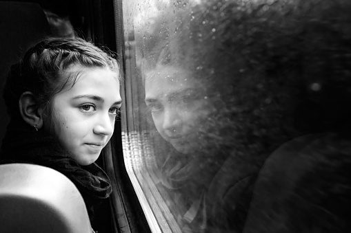 Little girl looking through window with reflections. She travels on a train.Rain drops on the window. Black and white image