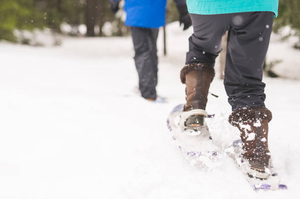 A senior couple heads out for a snowshoeing adventure in the white forest. The shot is from the rear and from their lower torso to their feet. There is copy space on the left side.