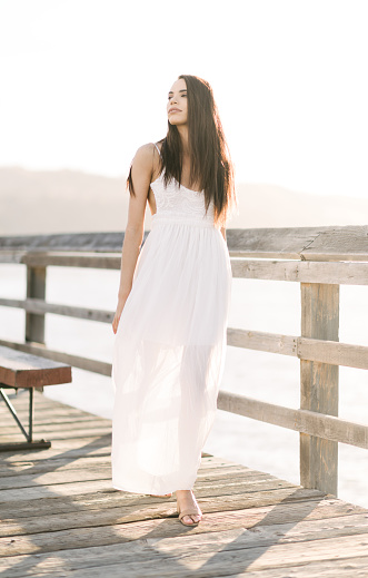 Confident young woman walking on a wooden pier during the golden hour sunset looking in to the distance.