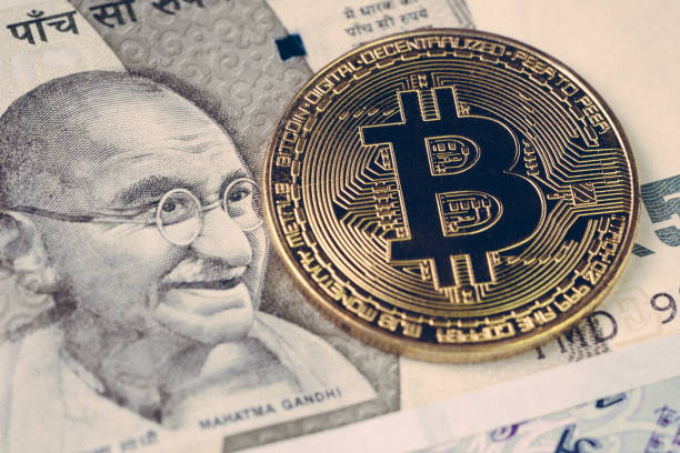 Bitcoin crypto currency banned in India concept, closed up shot of golden physical coin with B alphabet Bit coin sign on Indian rupee banknotes stock photo