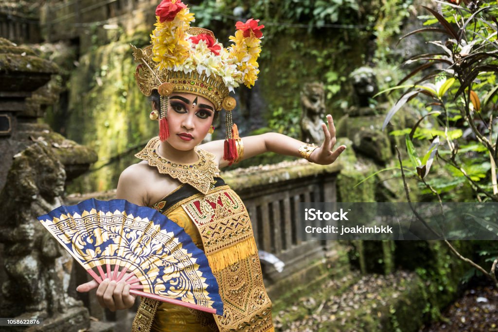 Young traditional Bali dancer in a bamboo forest A young teenage Balinese girl wearing a traditional Barong costume gracefully poses with a hand fan and dances in a Hindu temple. The Hindu culture is still well preserved and children learn at a very young age the art of Ramayana and dance. Ubud Stock Photo