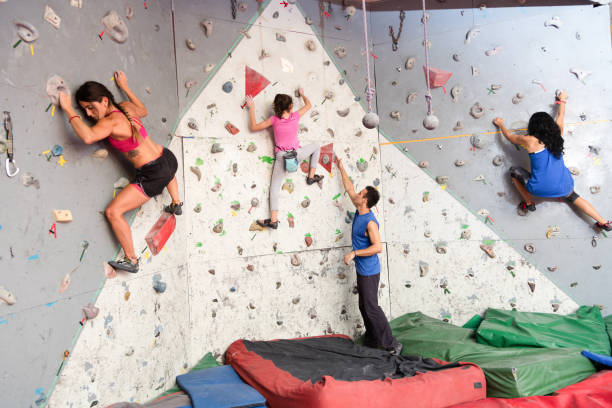 menina orientador de instrutor em um local de escalada e mulheres escalada nas laterais - climbing wall rock climbing holding reaching - fotografias e filmes do acervo