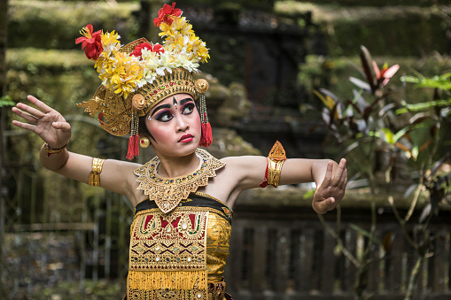 A young teenage Balinese girl wearing a traditional Barong costume gracefully poses and dances in a Hindu temple. The Hindu culture is still well preserved and children learn at a very young age the art of Ramayana and dance.