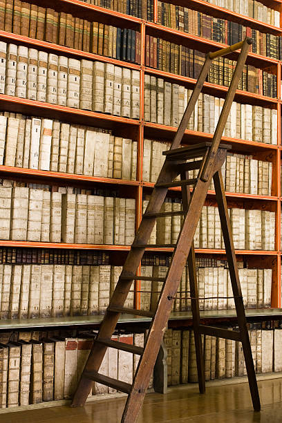 Shelves with old books in the library and wooden stepladder on the floor