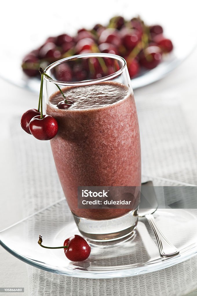 Cherry smoothie in a tall glass with a plate of cherries Cold cherry smoothie in glass close up Cherry Stock Photo