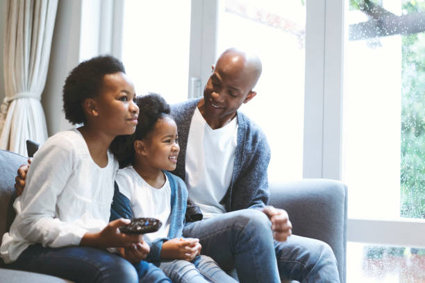 istock Smiling father and daughters watching TV at home 1058668644