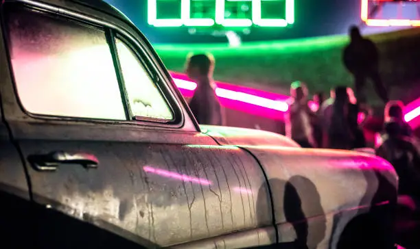 A fender from a 1950's American car, bathed in green and pink neon light.